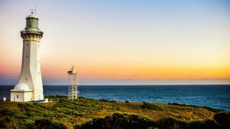 Serene Lighthouse at Sunset Overlooking Tranquil Waters wallpaper