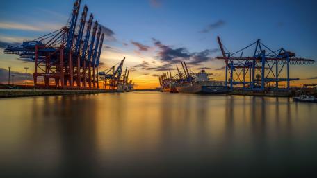 Serene Sunset Over Coastline Cranes and Ships wallpaper