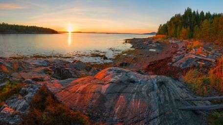 Serene Sunset Over Tranquil Waters and Rocky Shoreline wallpaper