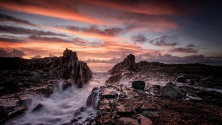Dramatic Sunset Over Rocky Coastline Waves wallpaper