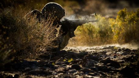 Soldier in Action Amidst Dusty Terrain and Brush wallpaper