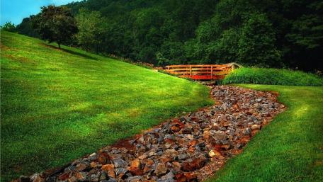 Lush Green Landscape with Rustic Bridge and Stream wallpaper