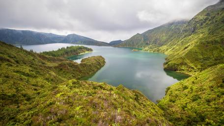 Serene Lake Surrounded by Lush Mountains and Clouds wallpaper