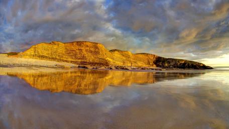 Golden Cliffs Reflected on Tranquil Coastline wallpaper