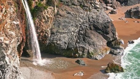 Majestic Waterfall Cascading into Serene Beach Scene wallpaper