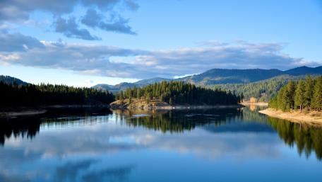 Serene Lake Reflection Surrounded by Lush Mountains and Blue Skies wallpaper