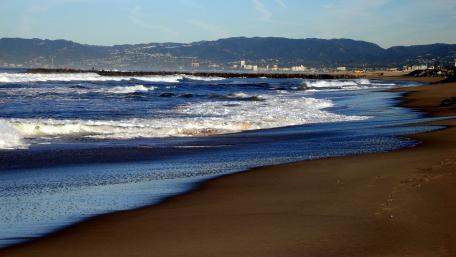 Serene Beachside Escape Amidst Gentle Waves and Mountains wallpaper