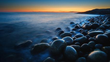 Serene Coastal Sunset Over Smooth Pebbles wallpaper