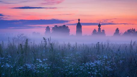 Mystical Dawn Over Misty Fields and Silhouetted Towers wallpaper