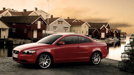 Sleek Red Car Against Charming Coastal Village Background wallpaper