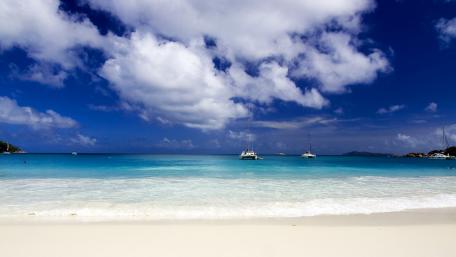 Tranquil Beach Paradise with Sailboats and Blue Skies wallpaper
