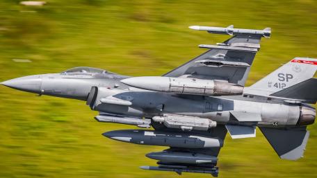 Fighter Jet in Action Above Green Landscape wallpaper