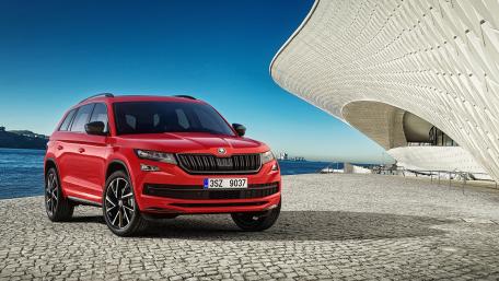 Dynamic Red SUV Against Modern Architecture in Bright Blue Sky wallpaper