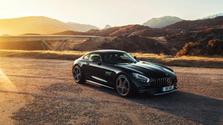 Sleek Black Sports Car Under Golden Sunset Shadows wallpaper