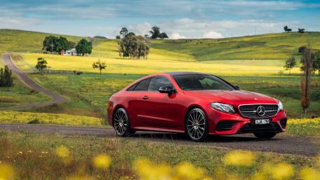 Red Luxury Car on Scenic Roadway Amidst Fields of Yellow Flowers wallpaper