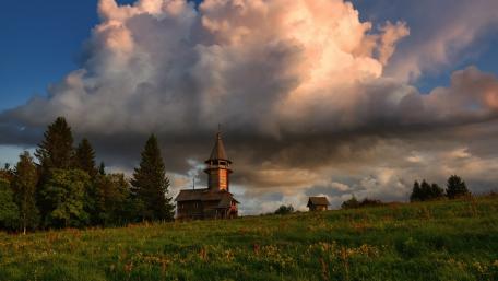 Serene Landscape with Towering Clouds and Cozy Cabin wallpaper