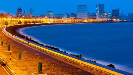 Serene Cityscape at Dusk with Calm Waters and Lights Illuminating the Pathway wallpaper