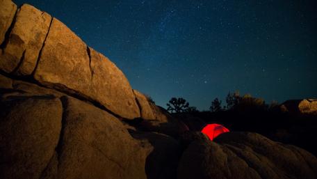 Starlit Night over Rocky Terrain with Tent Glow wallpaper