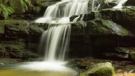 Serene Waterfall Flowing Through Lush Greenery wallpaper
