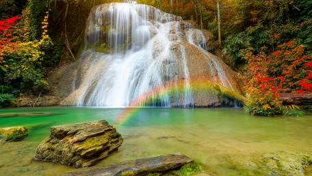 Majestic Waterfall with Rainbow Over Boulders wallpaper