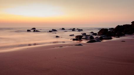 Tranquil Beach at Sunset with Rocks and Horizon Glow wallpaper