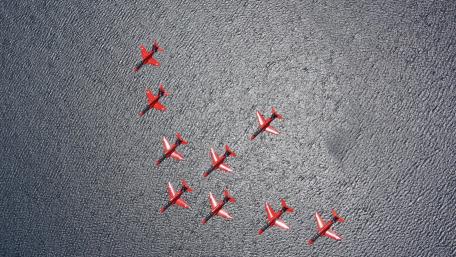 Dynamic Aerial Formation of Red Airplanes Over Water wallpaper