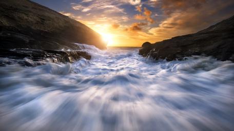 Majestic Sunset Over a Rapid River Flowing Between Rocks wallpaper