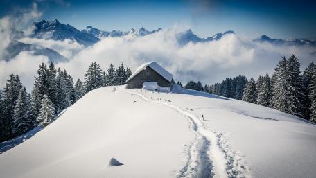 Serene Winter Cottage Amidst Majestic Mountains wallpaper