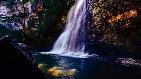 Serene Waterfall Amidst Majestic Cliffs and Rocks wallpaper