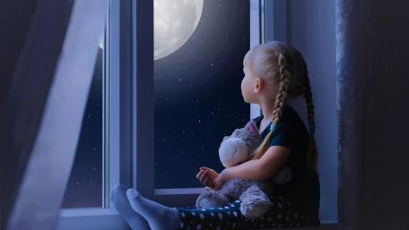 Little girl sadly out of a window with a teddy bear wallpaper
