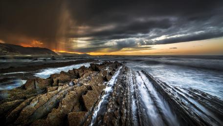Stormy Sunset Over Rocky Shoreline wallpaper