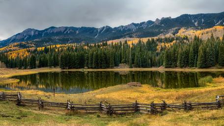 Serene Pond Surrounded by Majestic Mountains and Vibrant Trees wallpaper