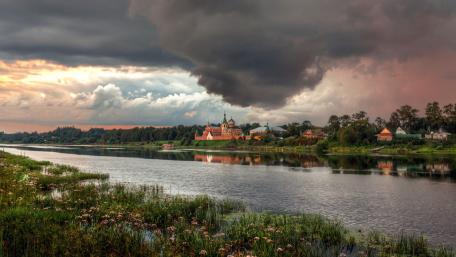 Serene Village by the River Under Cloudy Skies wallpaper