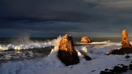 Stormy Waves Crashing Against Rugged Rocks in Twilight wallpaper