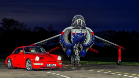 Red Porsche in Front of Military Aircraft Showcase Night Scene wallpaper
