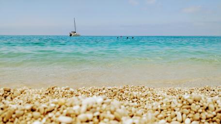 Serene Beachfront with Gentle Waves and a Sailboat wallpaper