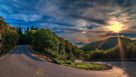 Curvy Road Through Serene Mountains Under Cloudy Sky wallpaper