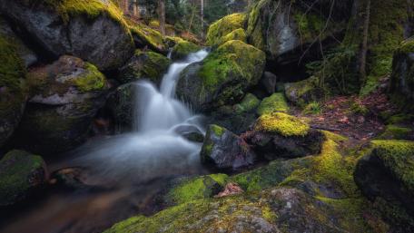 Serene Waterfall Amid Mossy Stones and Boulders wallpaper