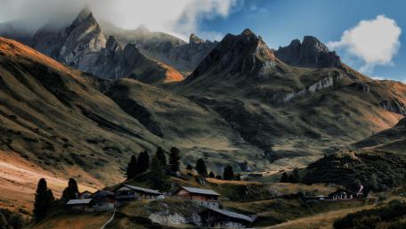 Serene Mountain Cottage Amidst Majestic Peaks wallpaper