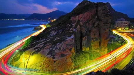Vibrant Light Trails Along Coastal Roadway wallpaper