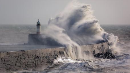 Majestic Lighthouse Amidst Fierce Storm Waves wallpaper