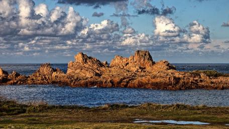 Serene Coastal Rocks Under Fluffy Clouds wallpaper