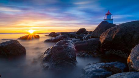 Serene Sunset by the Lighthouse on Rocky Shoreline wallpaper