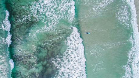 Serene Aerial View of Ocean Waves and Surfers wallpaper