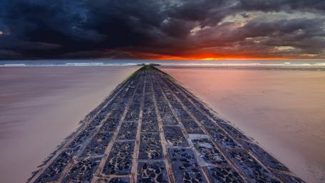 Mysterious Beach Pathway Under Dark Clouds wallpaper