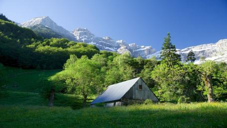 Mountain Cottage Surrounded by Lush Greenery and Majestic Peaks wallpaper