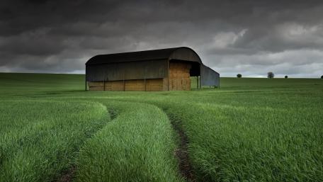 Serene Barn in Lush Green Field Under Cloudy Sky wallpaper