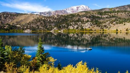 Serene Lake Reflection with a Motorboat Riding Through Calm Waters wallpaper