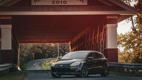 Sleek Black Car Under a Rustic Bridge wallpaper