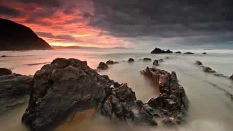 Dramatic Coastal Sunset Over Rugged Rocks wallpaper